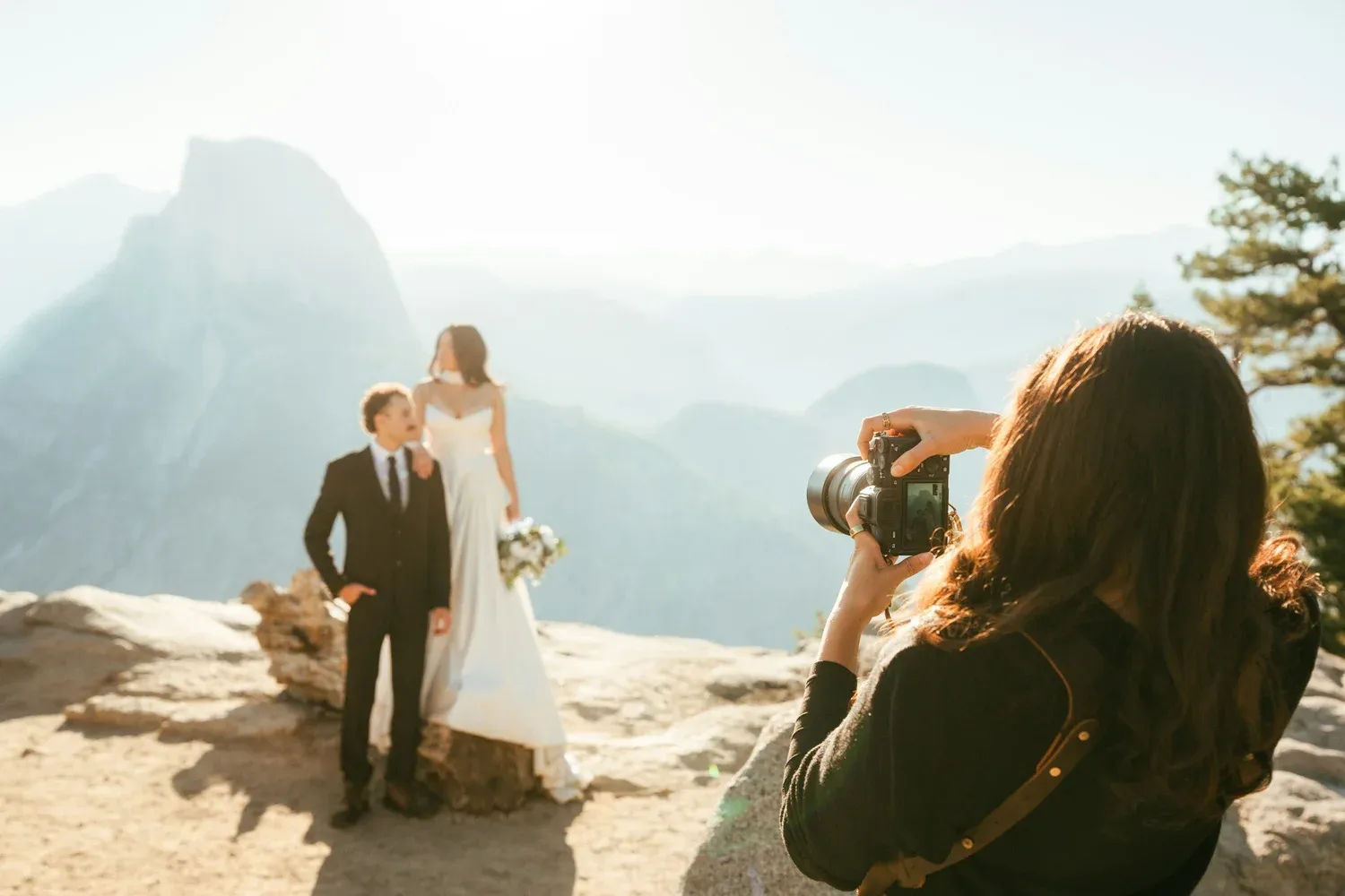 Photographer taking a picture of a bride and groom on a rocky mountain overlook.